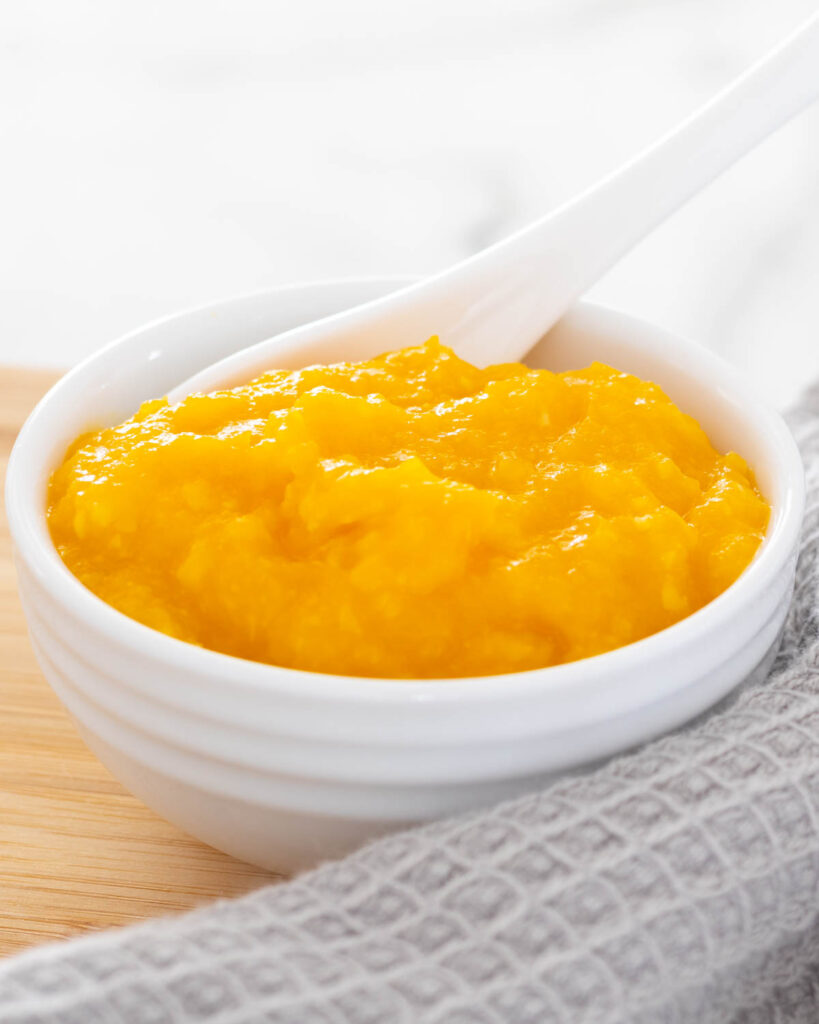 Apple, Pumpkin and Sweet Corn Puree served for baby in a small white ramekin with spoon.