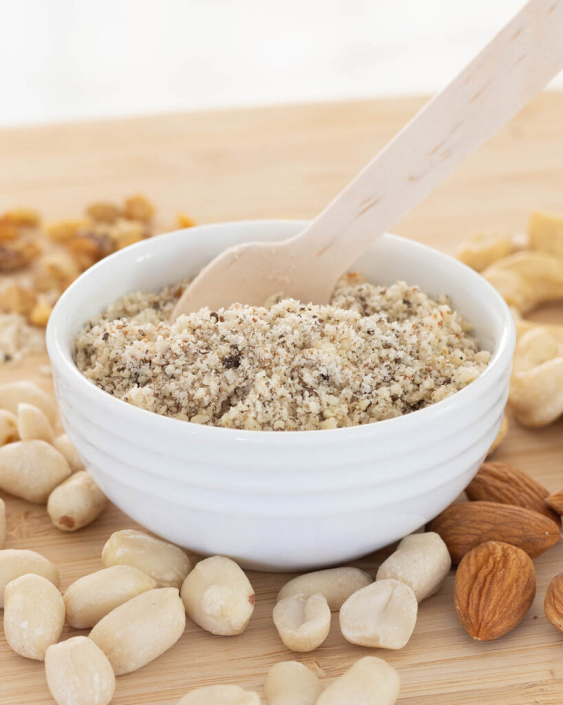 Nut and Seed Sprinkle in a small ramekin showing it's very fine texture, surrounded by whole nuts.