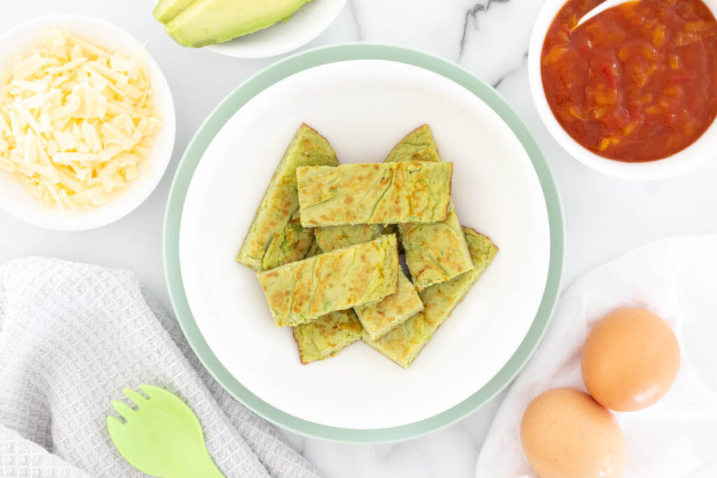 Avocado Omelette served for baby in strips, with cheese, avocado, relish and eggs surrounding the plate.