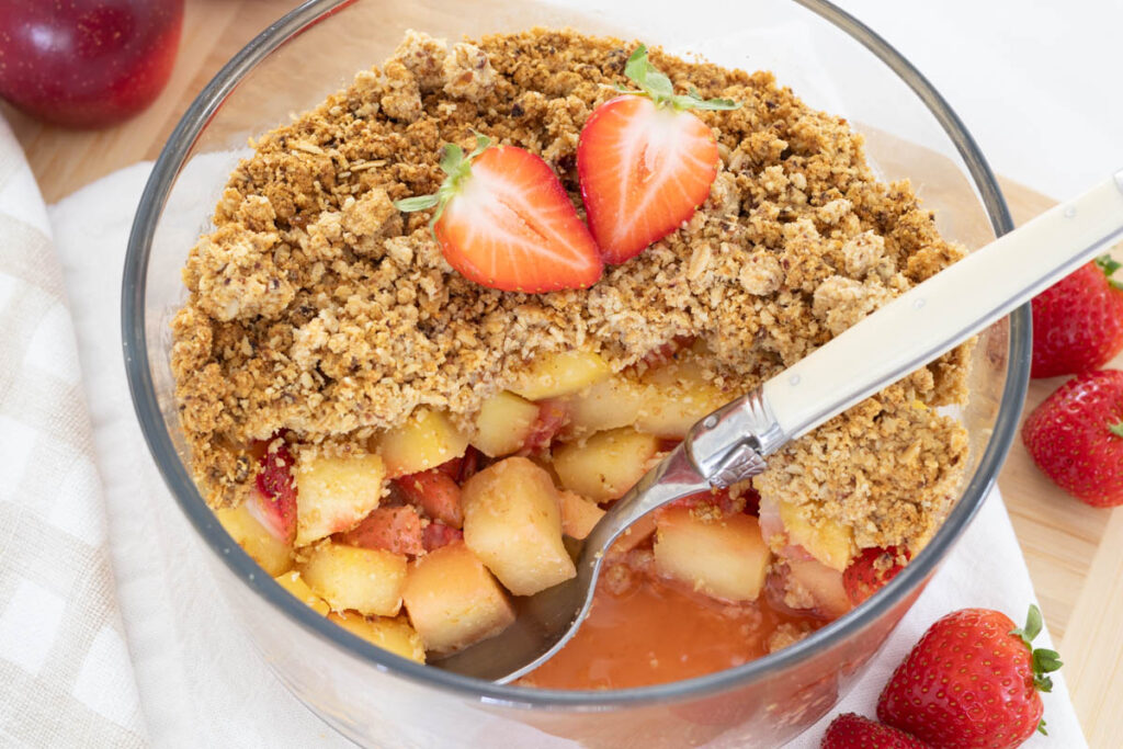 Strawberry and Apple Crumble with some spooned out from dish, to show stewed fruit inside.