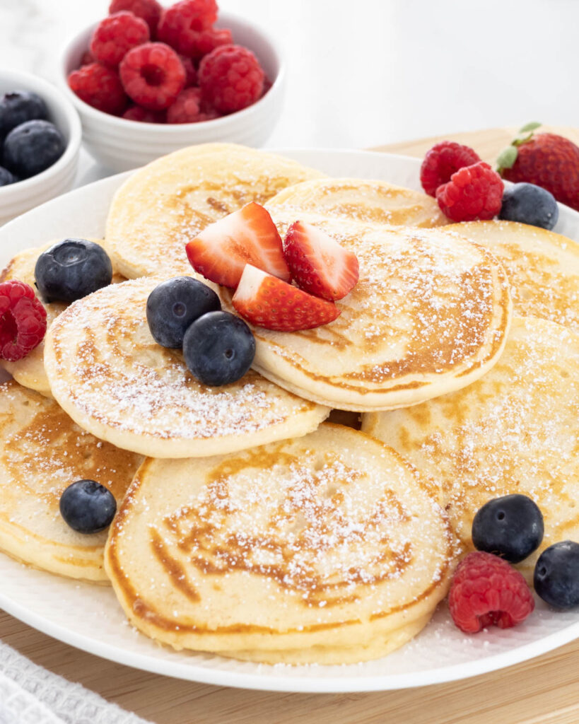 Small Batch Pancakes piled on a plate, dusted with icing sugar and topped with fresh berries.