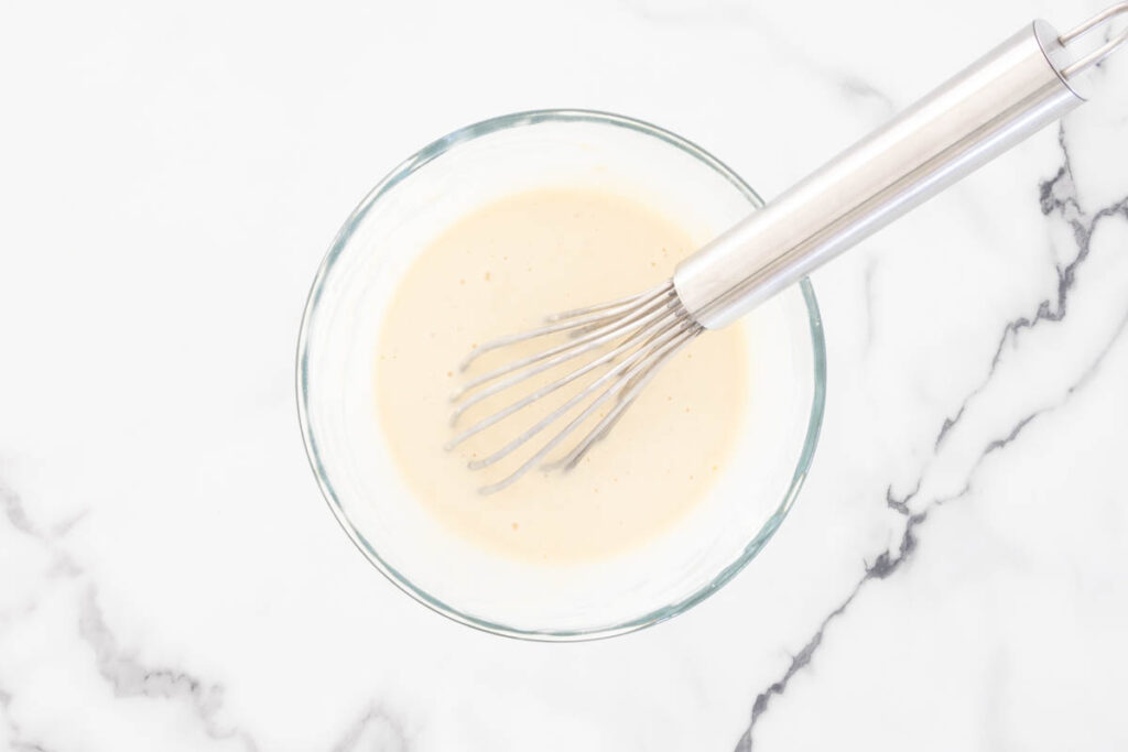 The whisked pancake batter in a glass bowl.