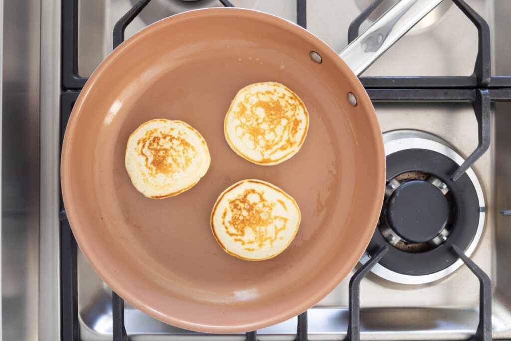 Three golden Mini Pancakes cooking in a frypan.